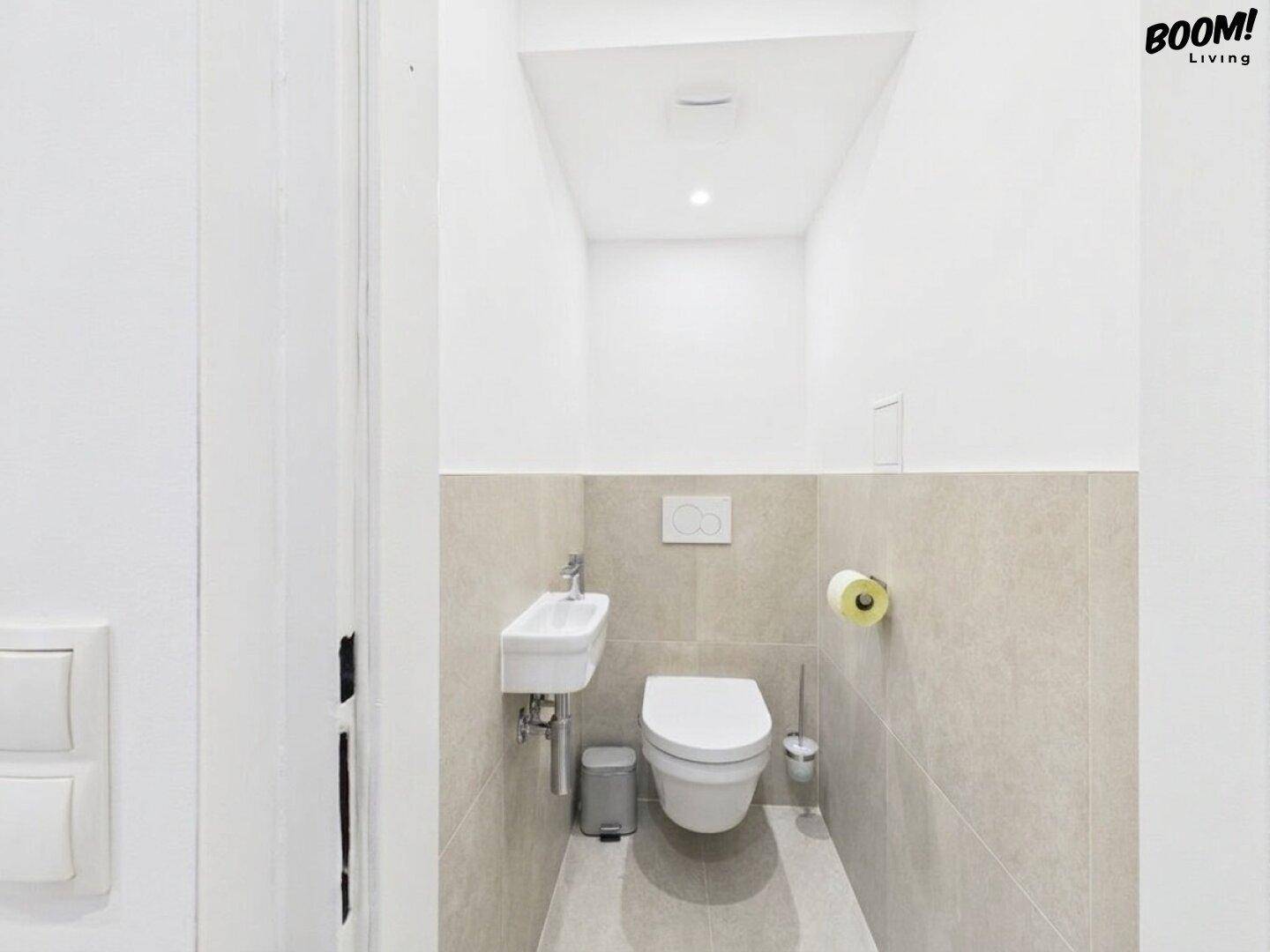 Modernes Gäste-WC mit wandhängender Toilette, kleinem Waschbecken und hellen Fliesen.