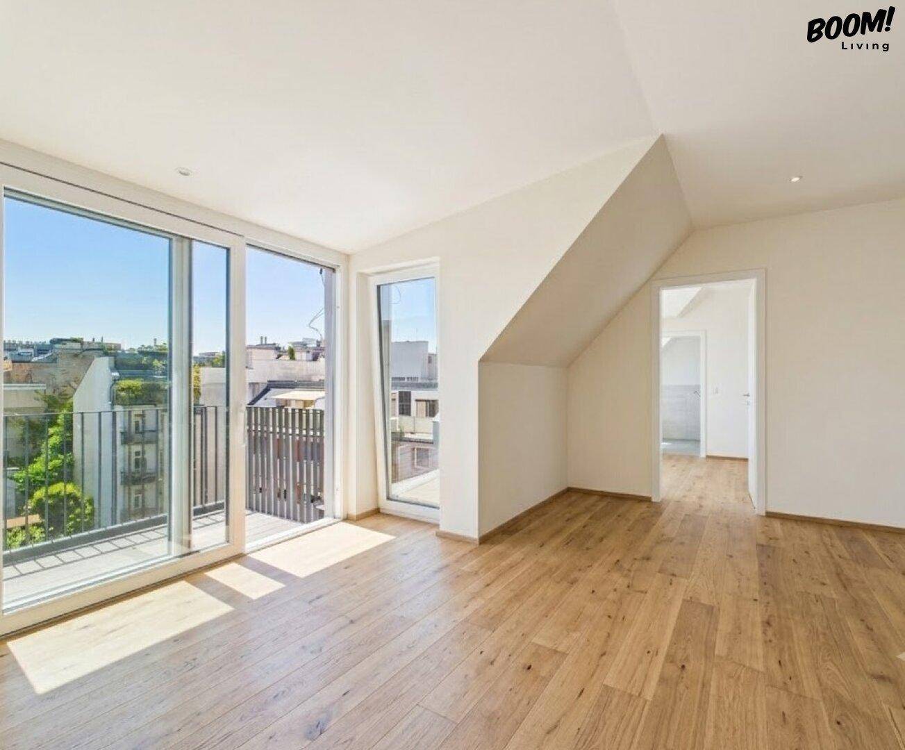 Lichtdurchfluteter Raum mit Holzboden, Zugang zum Balkon und schrägen Decken im Dachgeschoss.