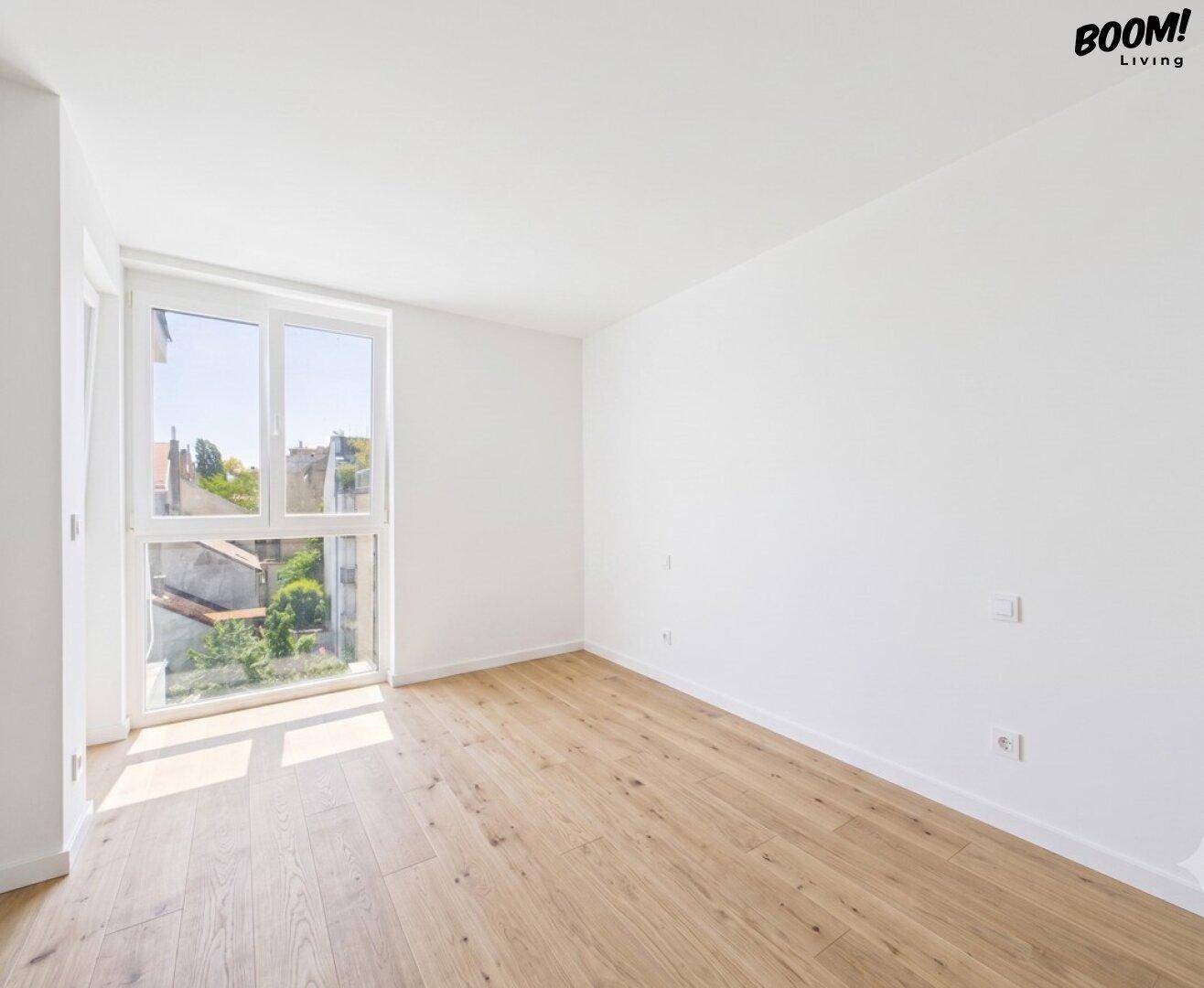 Helles Schlafzimmer mit Holzboden, weißen Wänden und großem Fenster mit Blick ins Grüne.