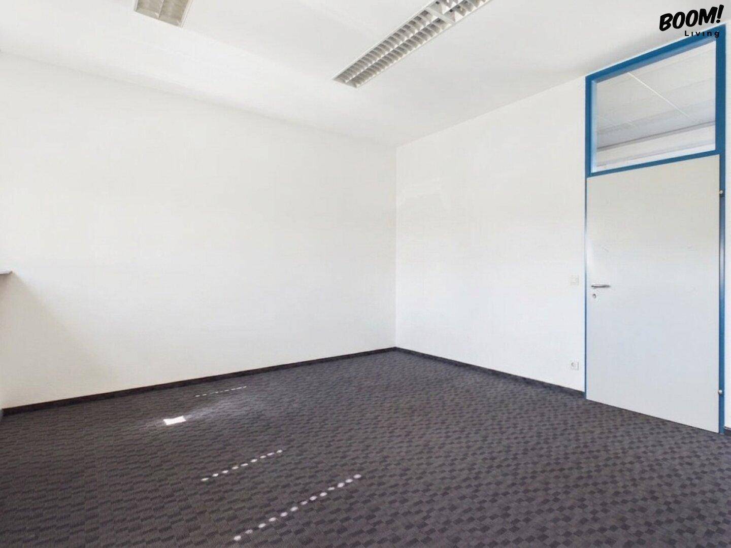 Leeres Büro mit Teppichboden, weißen Wänden und einer Tür mit blauem Rahmen.