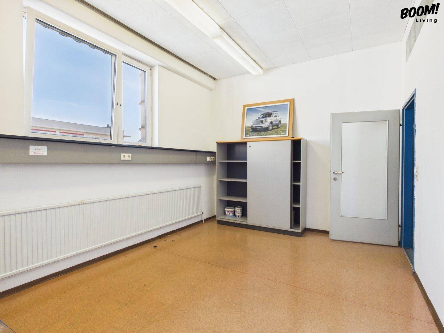 Büro mit Fenster, Schrank und einer Tür, die zu einem anderen Raum führt.