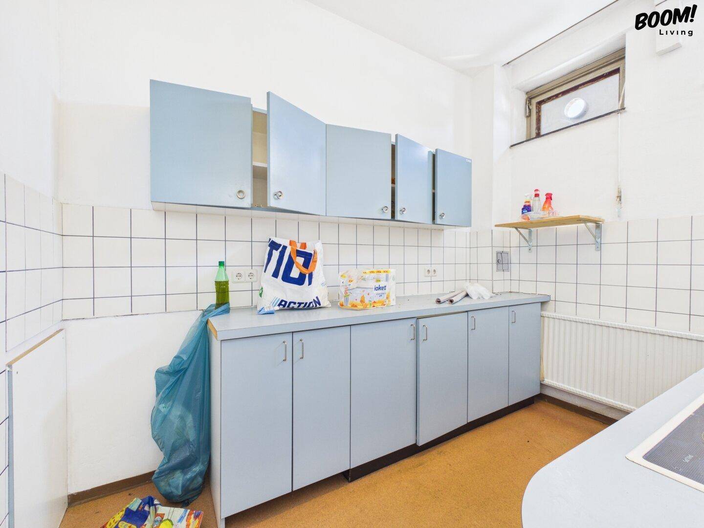 Einfache Küche mit hellblauen Schränken, weißen Fliesen und einem Fenster.