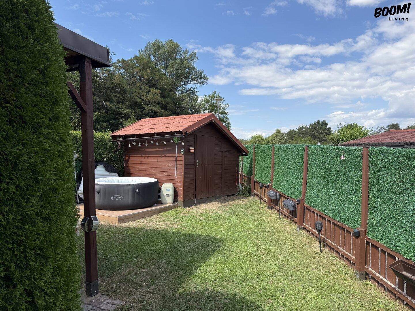 Gartenbereich mit einem aufblasbaren Whirlpool auf einer Holzplattform und einem kleinen Geräteschuppen.