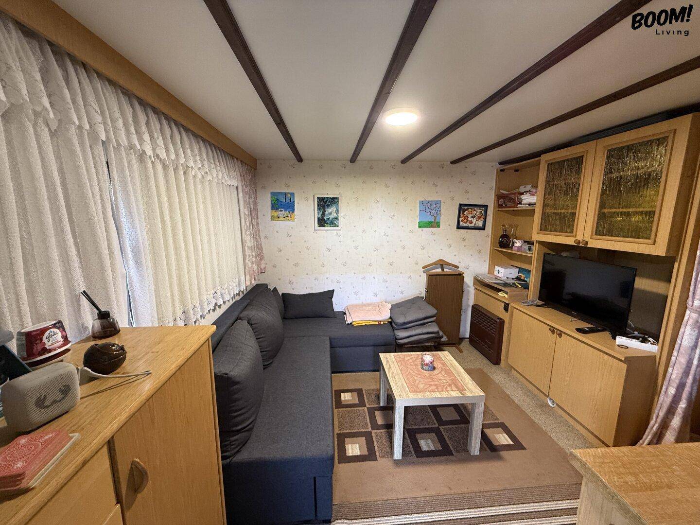 Gemütliches Wohnzimmer mit dunklem Ecksofa, Couchtisch und einem TV-Möbel unter sichtbaren Deckenbalken.