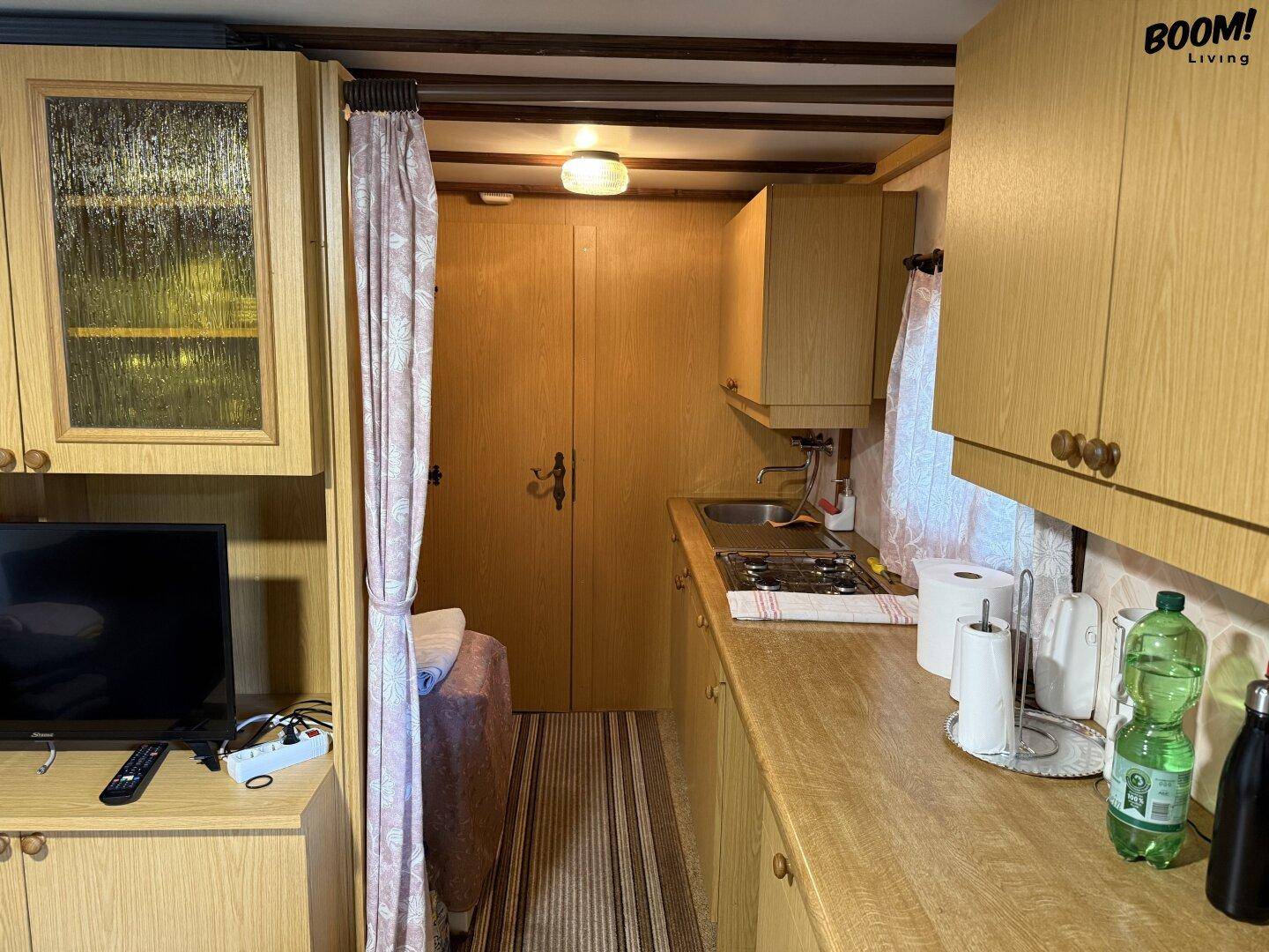 Kleine Küchenzeile mit Spüle und Kochfeld, integriert in Holzschränke, abgetrennt vom Schlafbereich.