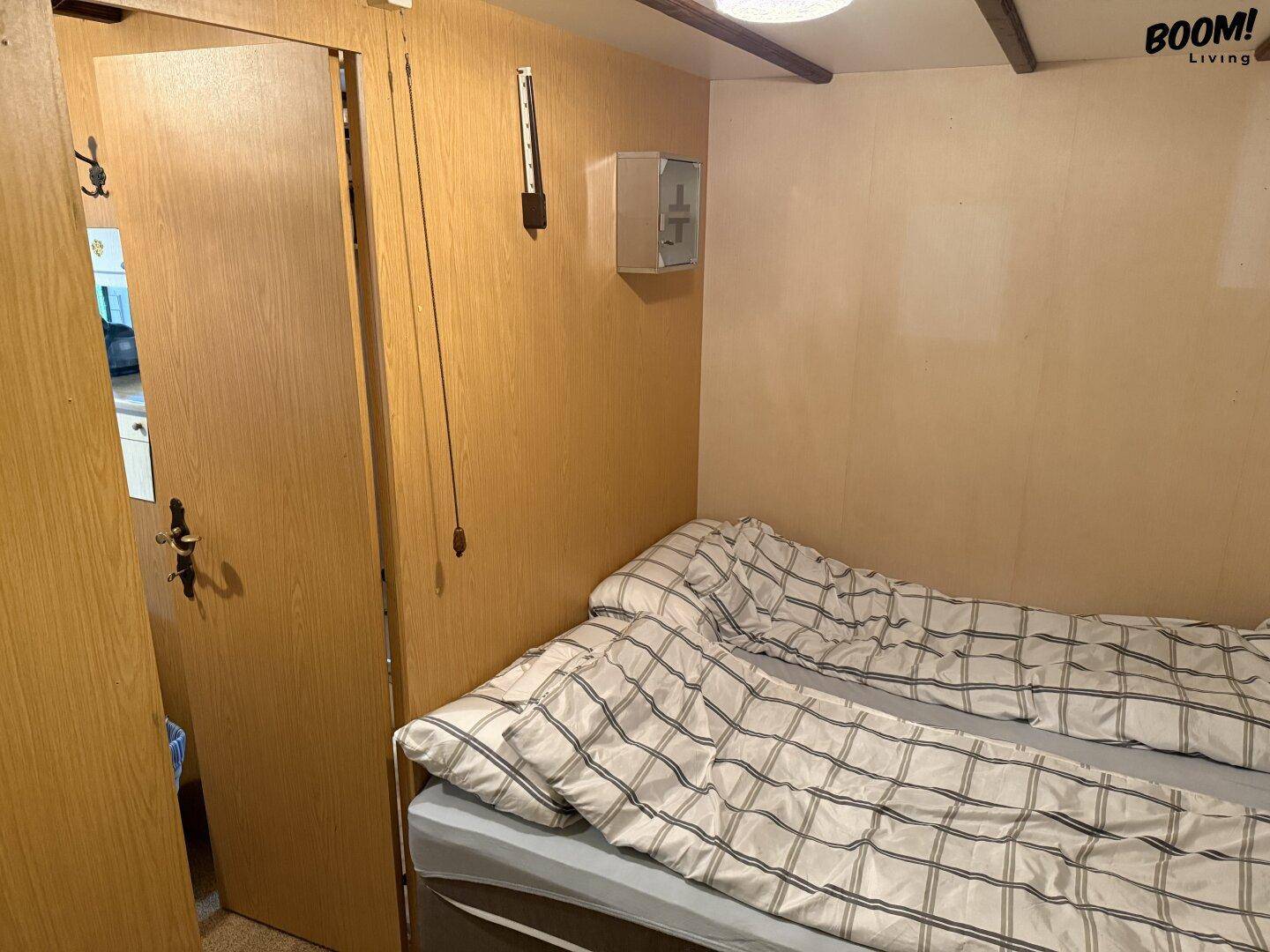 Kleines Schlafzimmer mit einem Bett und holzvertäfelten Wänden, einfach und funktional eingerichtet.