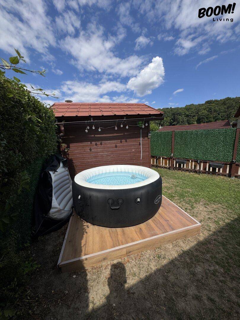 Aufblasbarer Whirlpool auf einer Holzplattform im Garten, umgeben von grüner Natur unter blauem Himmel.