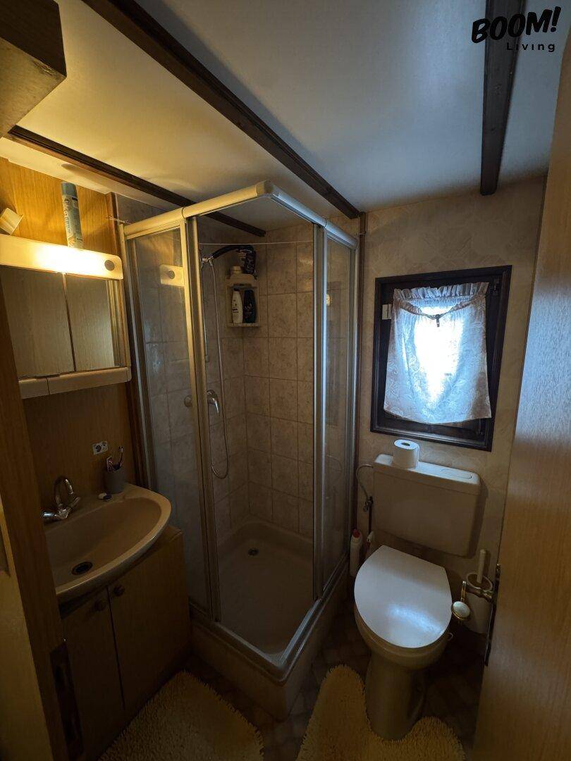 Kleines Badezimmer mit Duschkabine, Toilette und Waschbecken, funktional und einfach gefliest.