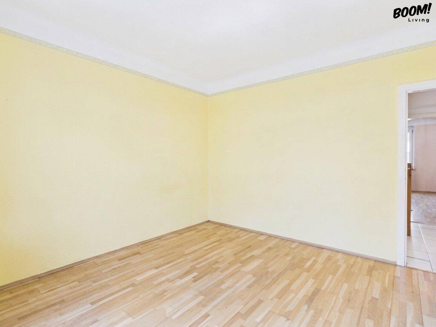 Leeres Zimmer mit gelben Wänden und Parkettboden, bereit zur individuellen Gestaltung.
