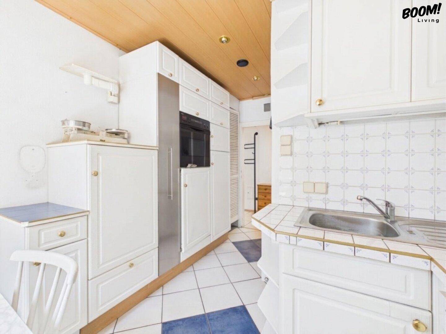 Funktionale Küche mit weißen Schränken, integriertem Kühlschrank und Holzdecke.