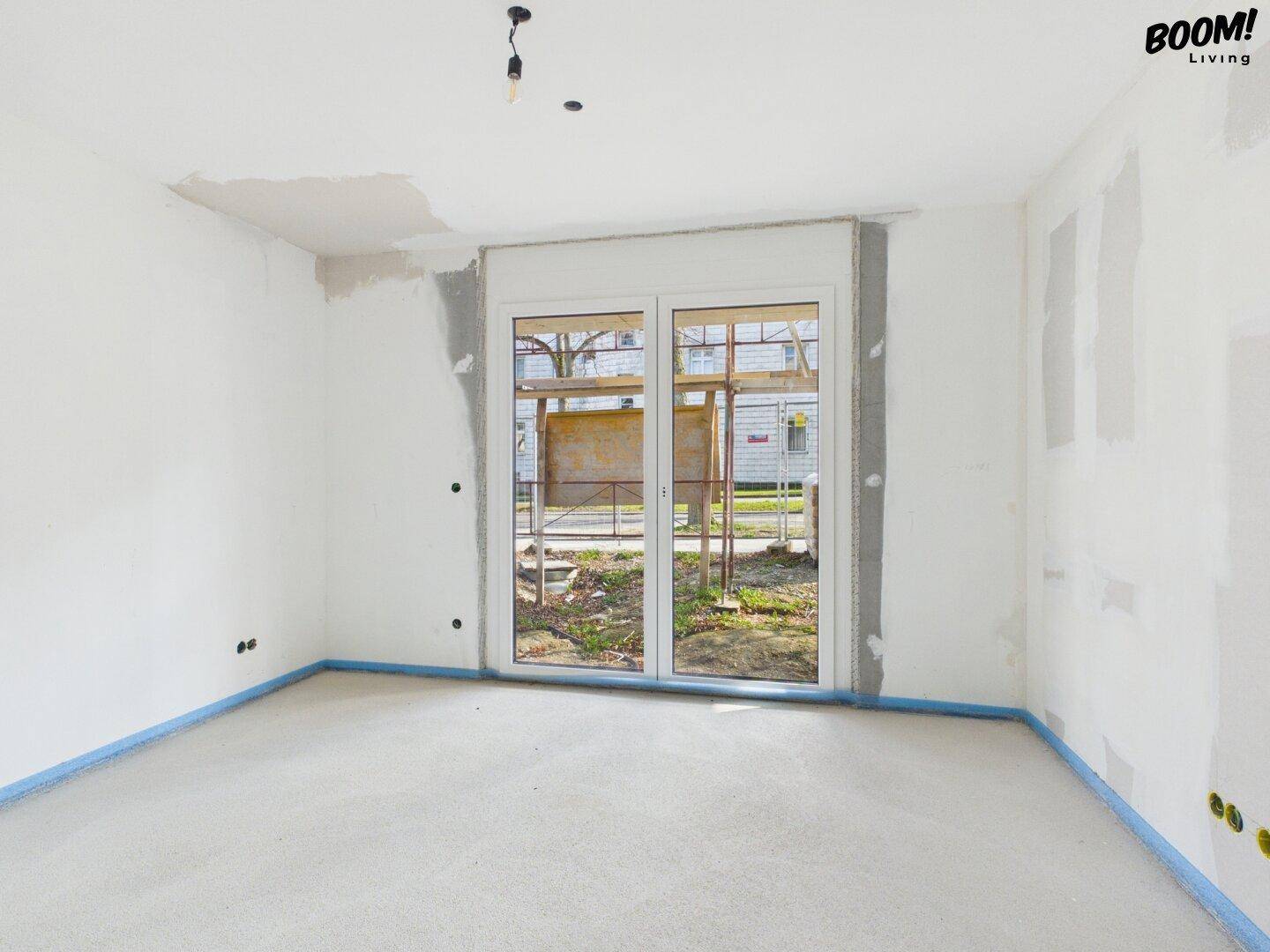 Heller Rohbau-Raum mit doppelter Glastür und Blick auf die zukünftige Außenanlage.