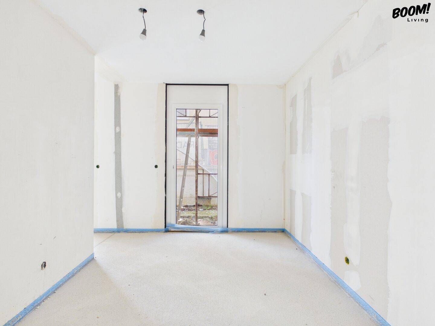Rohbau-Zimmer mit einer Glastür, die Zugang nach draußen bietet, und vorbereiteten Wänden.