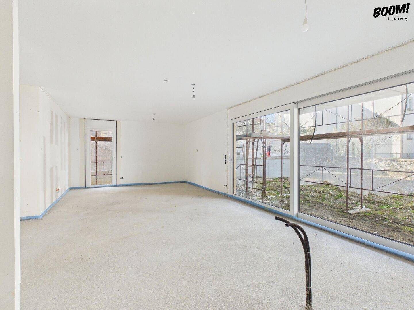 Heller, unfertiger Raum mit großen Schiebetüren und Blick auf die Außenanlage im Bau.