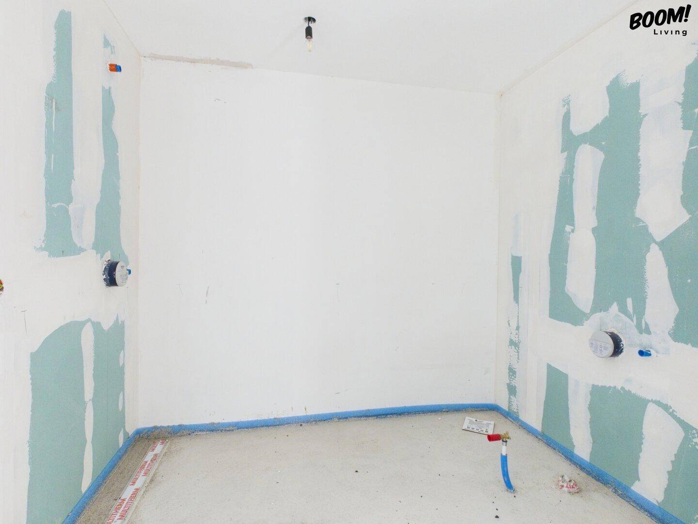 Rohbau-Badezimmer mit grünen Putzflächen und sichtbaren Wasseranschlüssen für Dusche oder Badewanne.