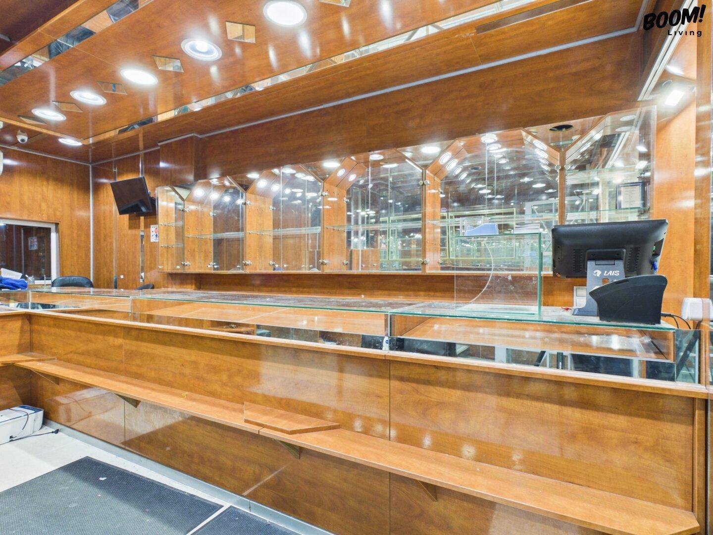 Detailansicht der Verkaufstheke in einem Ladenlokal mit Holzverkleidung, Glasplatte und Computerbildschirm.