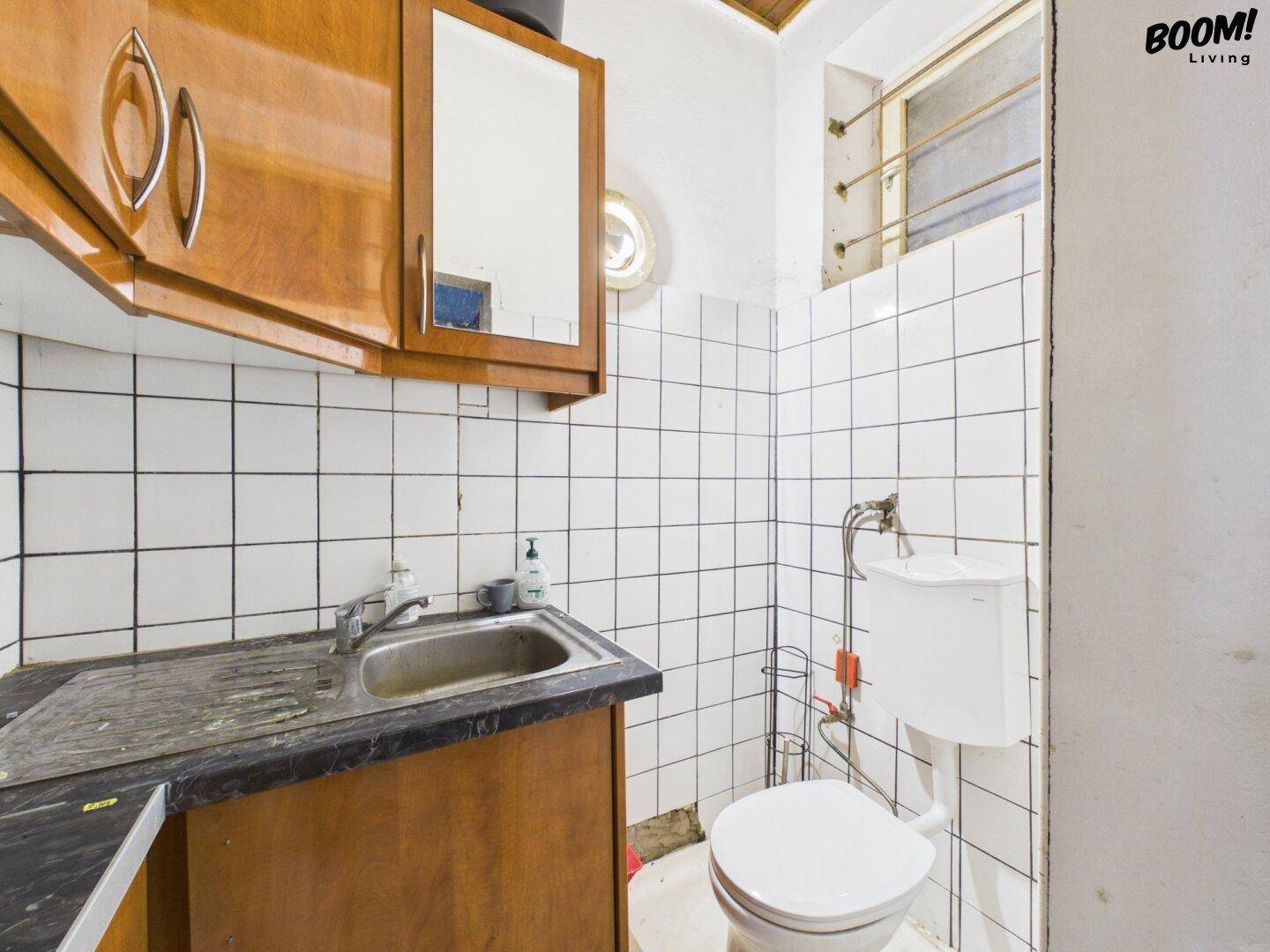 Kleiner, einfacher Toilettenraum mit Waschbecken, WC und gefliesten Wänden, renovierungsbedürftig.