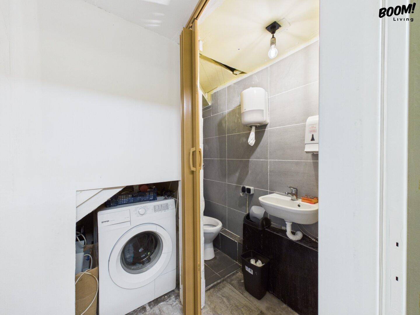 Kleine Toilette mit Waschbecken und Waschmaschine in einem separaten Bereich.