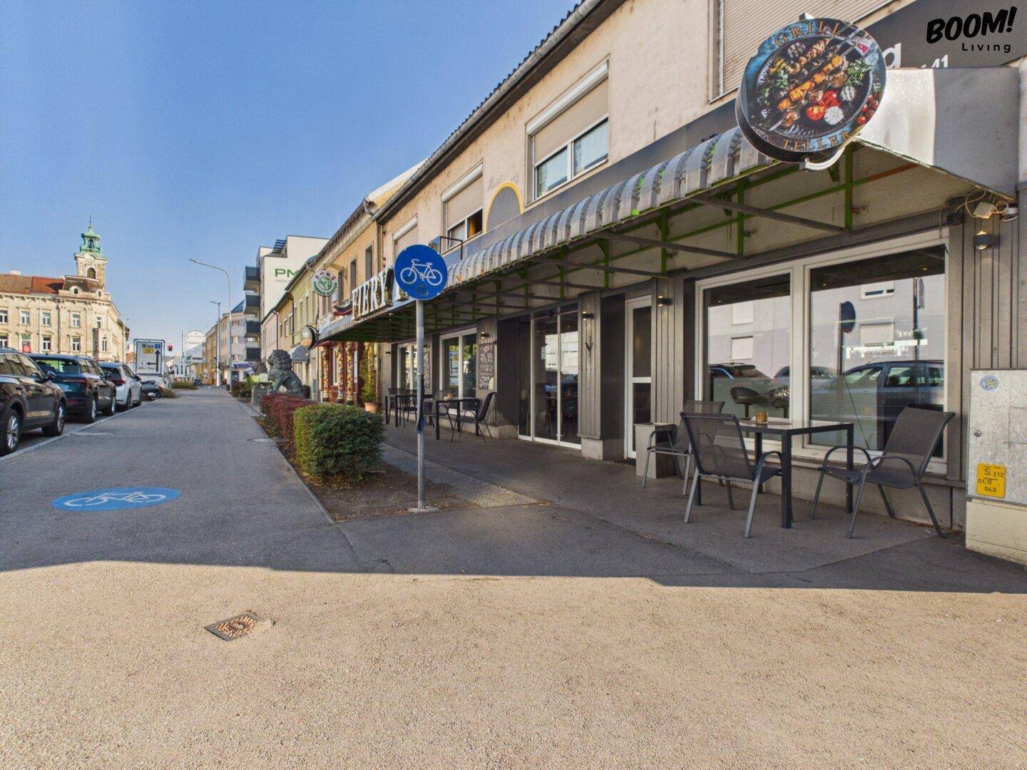 Seitenansicht des Restaurants mit Bürgersteig, Außentischen und einem Fahrradwegschild.
