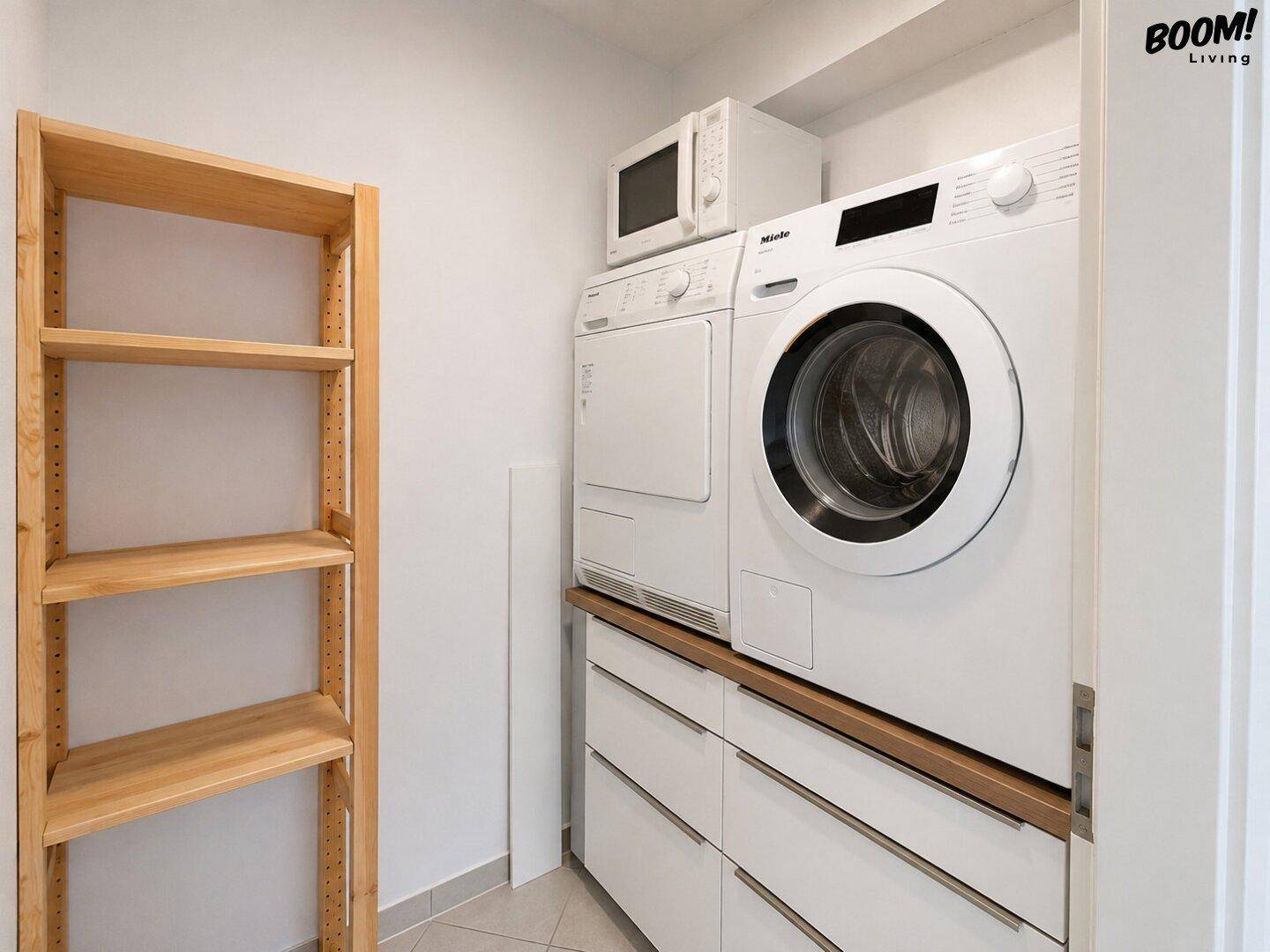 Praktischer Hauswirtschaftsraum mit Waschmaschine, Trockner, Mikrowelle und Regal.