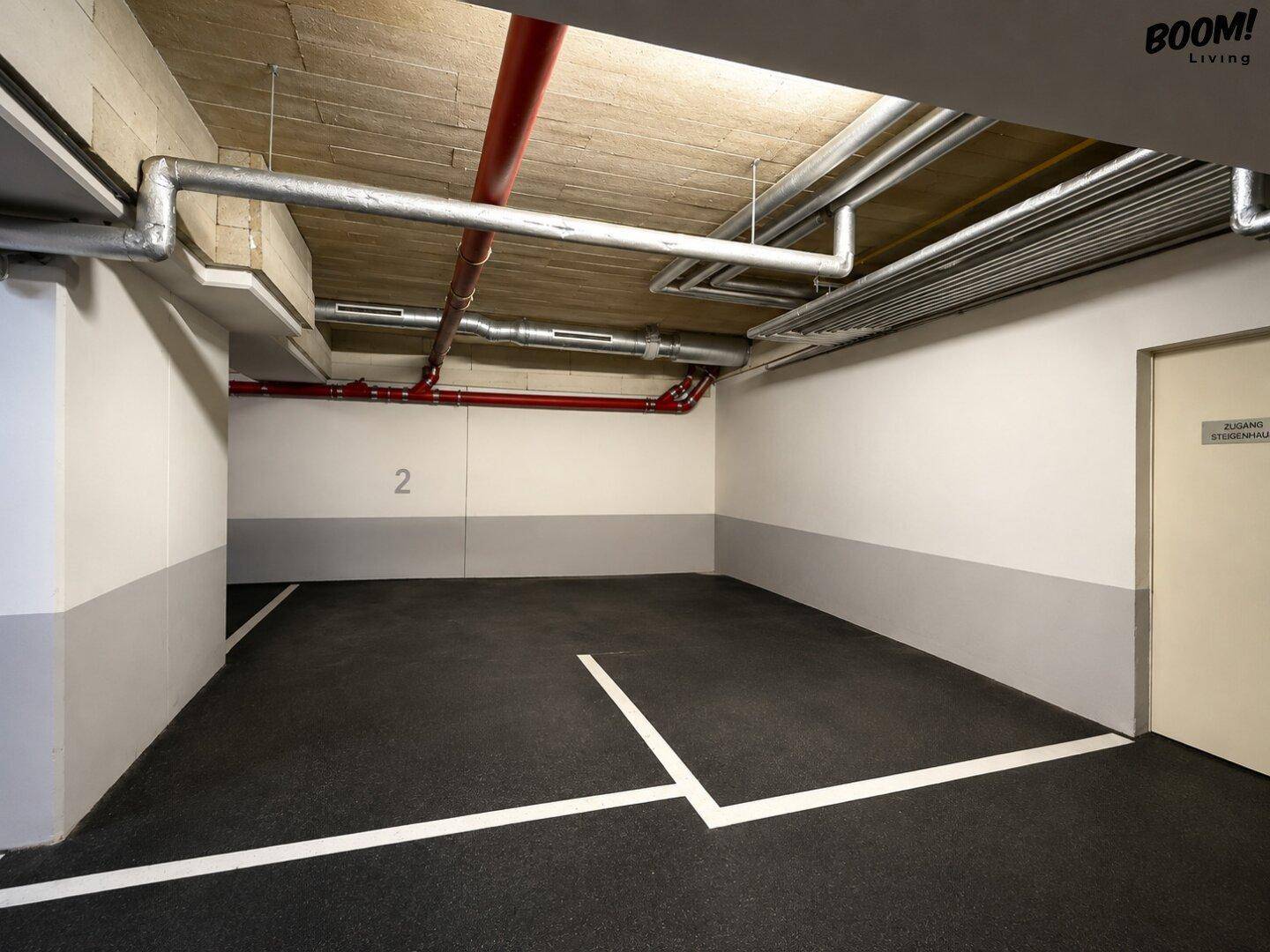 Tiefgarage mit markierten Stellplätzen und sichtbaren Versorgungsleitungen an der Decke.