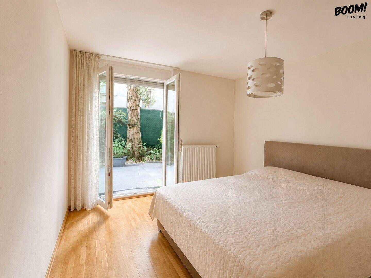 Schlafzimmer mit Holzboden und direktem Zugang zu einem kleinen, begrünten Außenbereich.