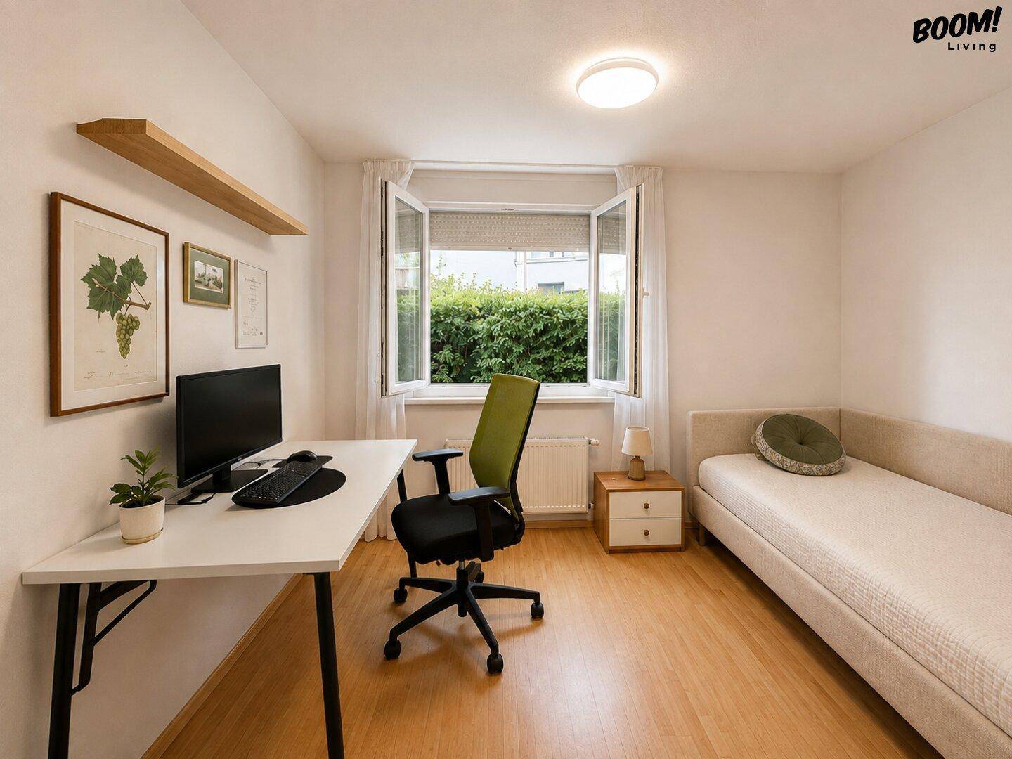 Helles Arbeitszimmer mit Schreibtisch, Einzelbett und Fenster mit Blick auf eine grüne Hecke.