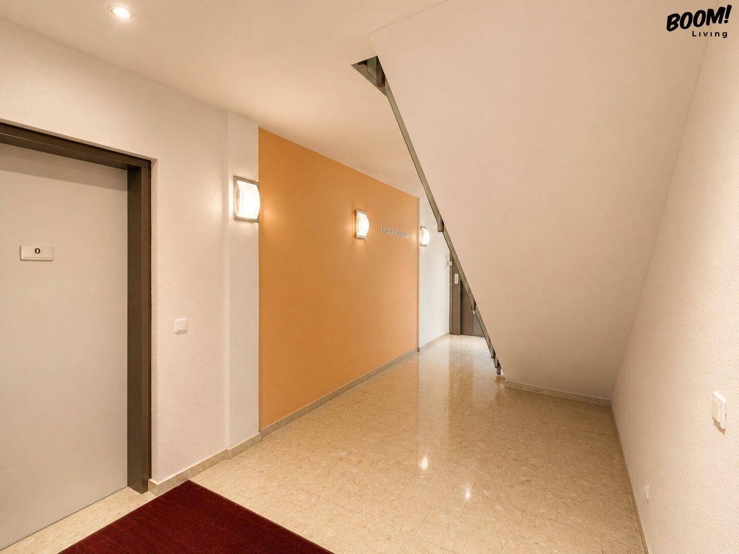 Moderner Flur mit Fliesenboden, orangefarbener Akzentwand und indirekter Beleuchtung.