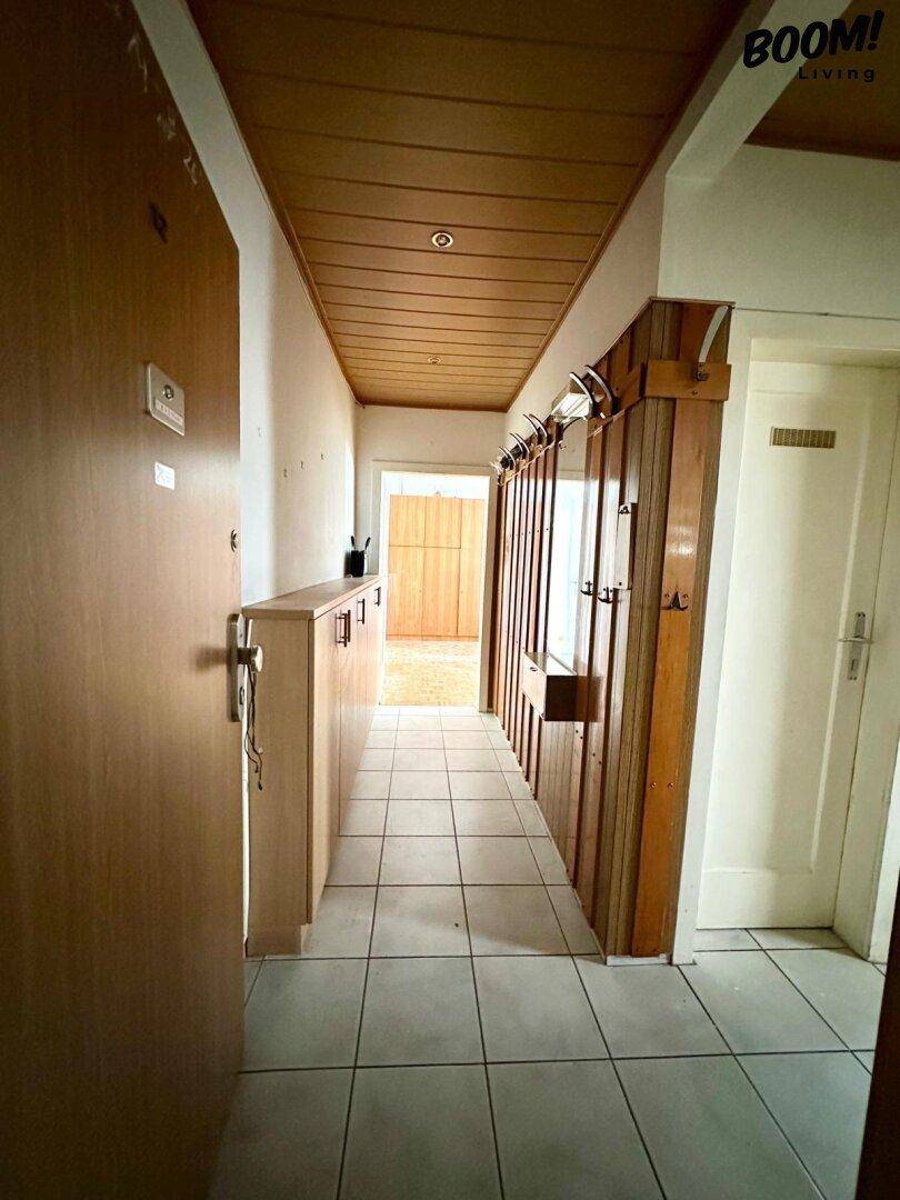 Langer Flur mit Holzdeckenverkleidung, Holzpaneelen an der Wand und hellen Fliesenboden.