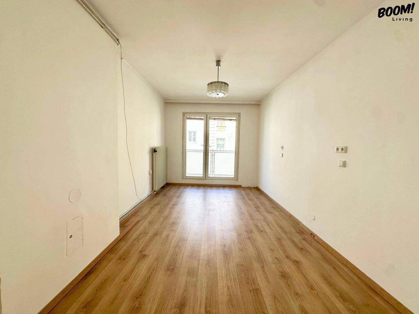 Heller Raum mit Laminatboden und einem französischen Balkon, der viel Tageslicht hereinlässt.