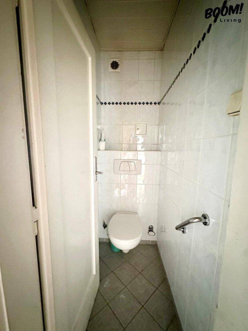 Kleines WC mit Wandfliesen, wandhängender Toilette und einem Haltegriff für zusätzliche Sicherheit.