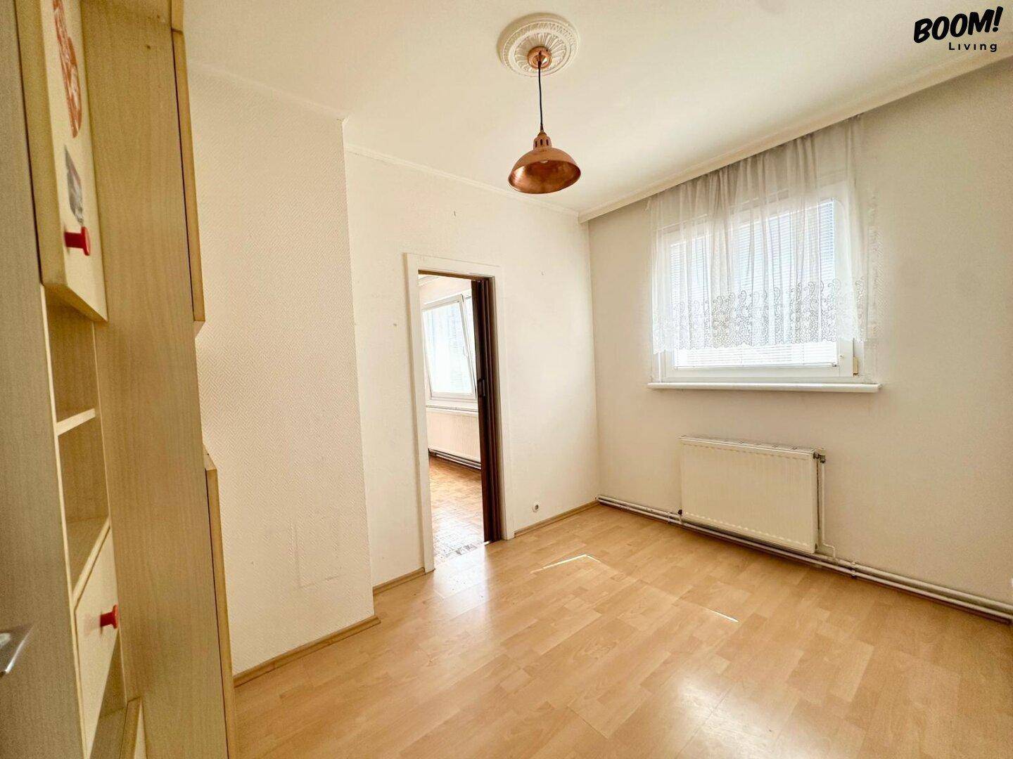 Schlafzimmer mit Laminatboden, weiß gestrichenen Wänden und einem Fenster für natürliches Licht.