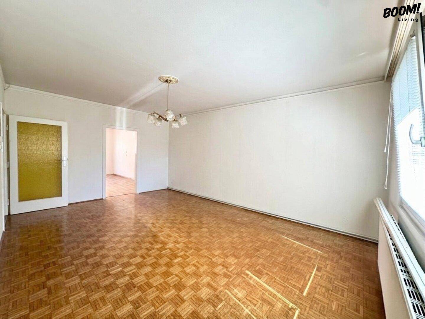 Helles Wohnzimmer mit Fischgrätparkett, weißen Wänden und einem klassischen Deckenleuchter.