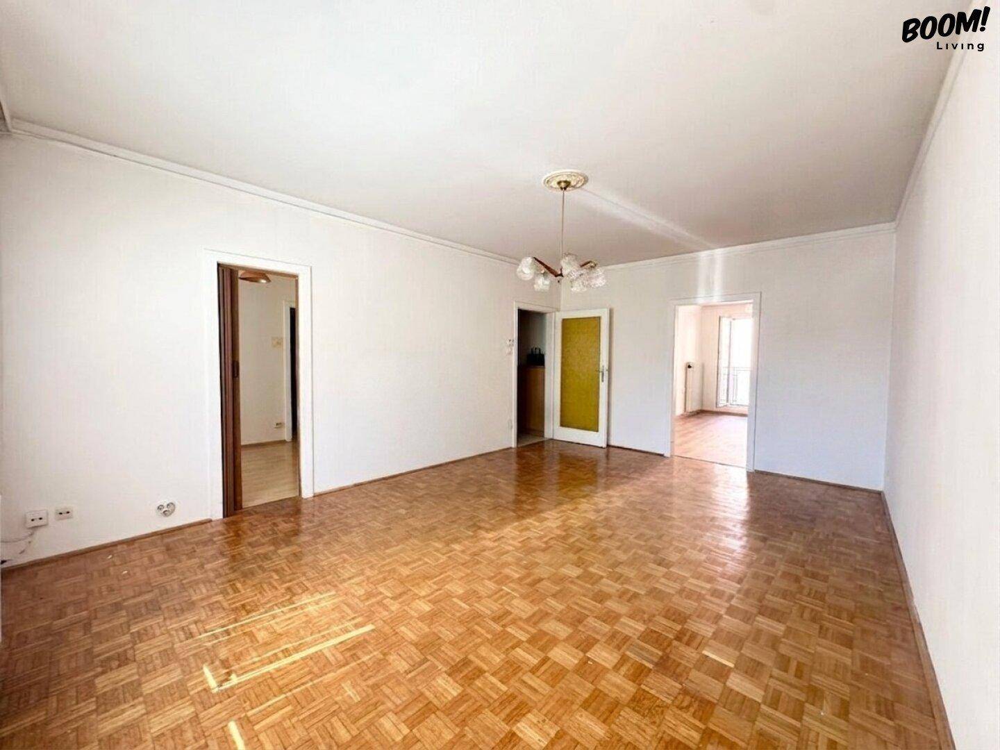 Geräumiges Wohnzimmer mit traditionellem Parkettboden und mehreren Zugängen zu anderen Räumen.