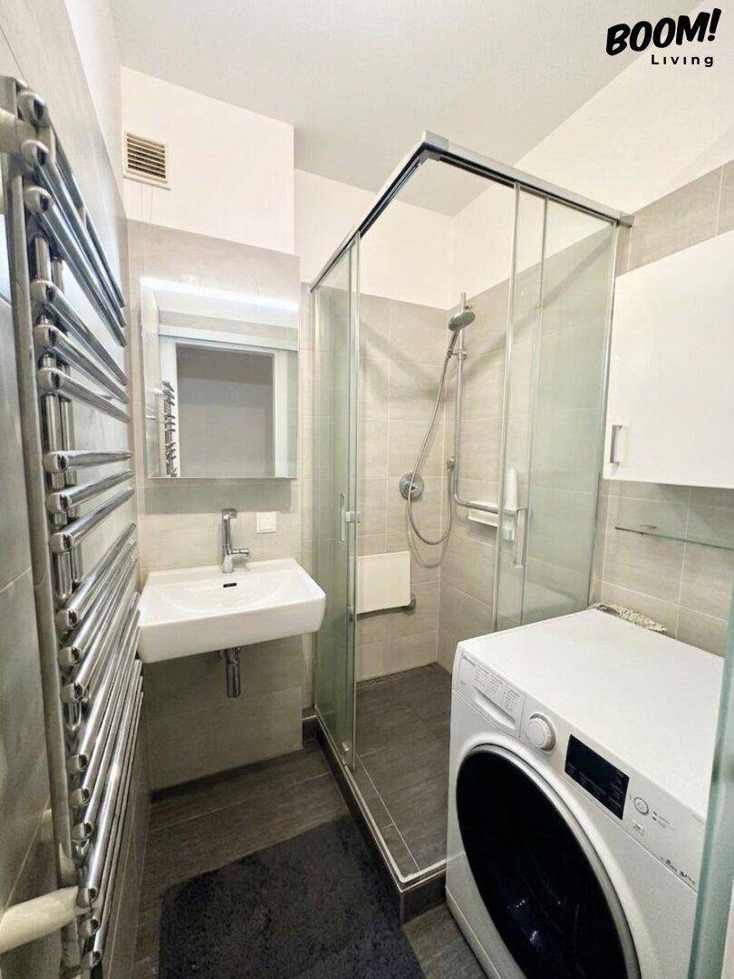 Modernes Badezimmer mit Duschkabine, Waschbecken, Waschmaschine und beheiztem Handtuchhalter.