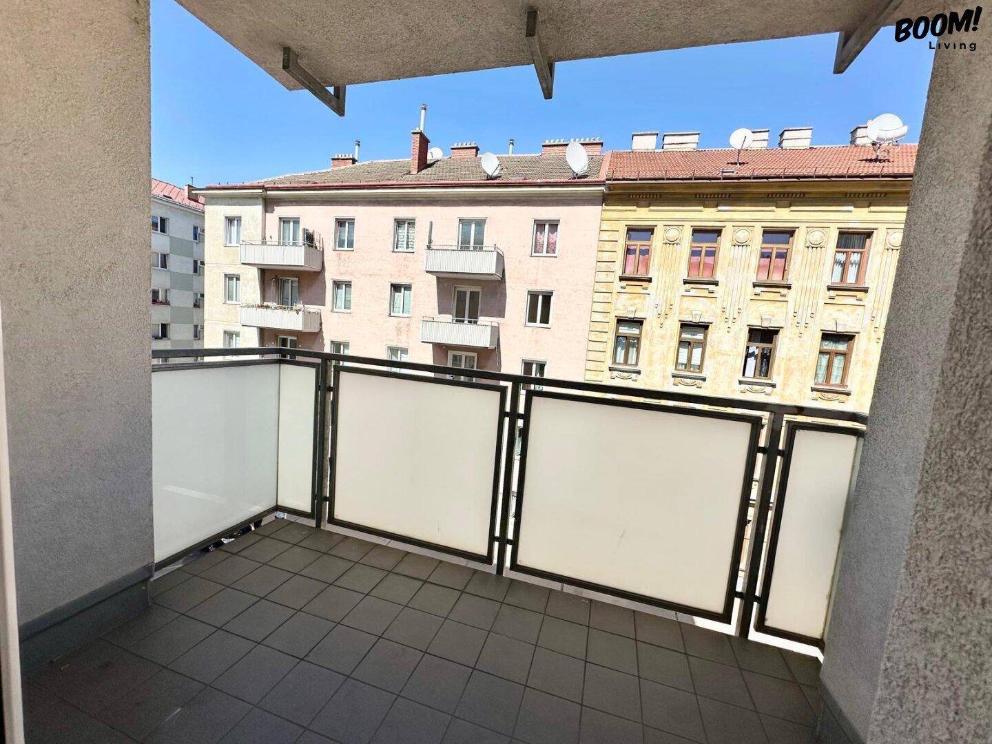 Geräumiger Balkon mit Fliesenboden und Blick auf die gegenüberliegenden Wohngebäude.