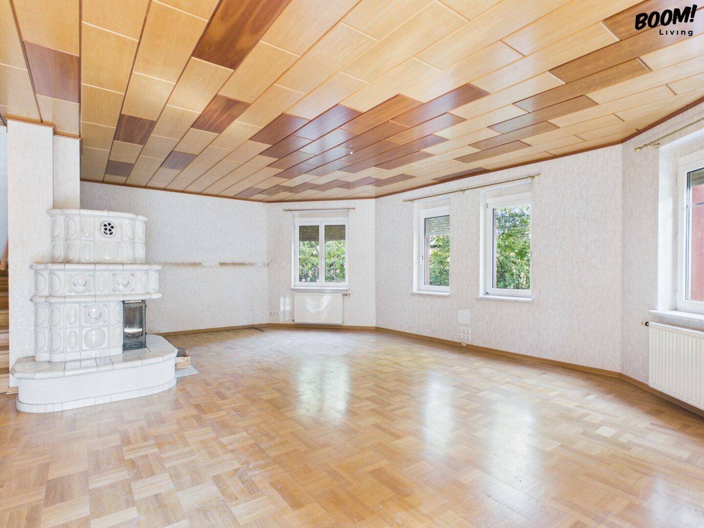 Heller Wohnbereich mit traditionellem Kachelofen, Parkettboden und Holzdecke, ideal für gemütliche Stunden.