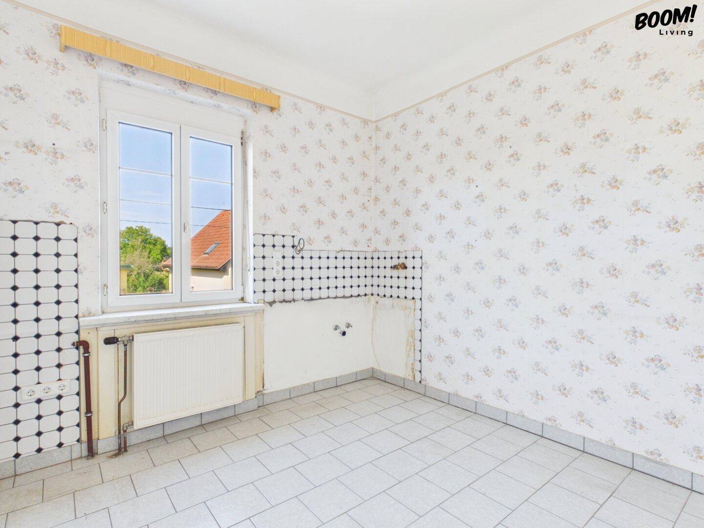 Leere Küche mit Fliesenboden und Fenster, bereit für die Installation einer neuen Einbauküche.