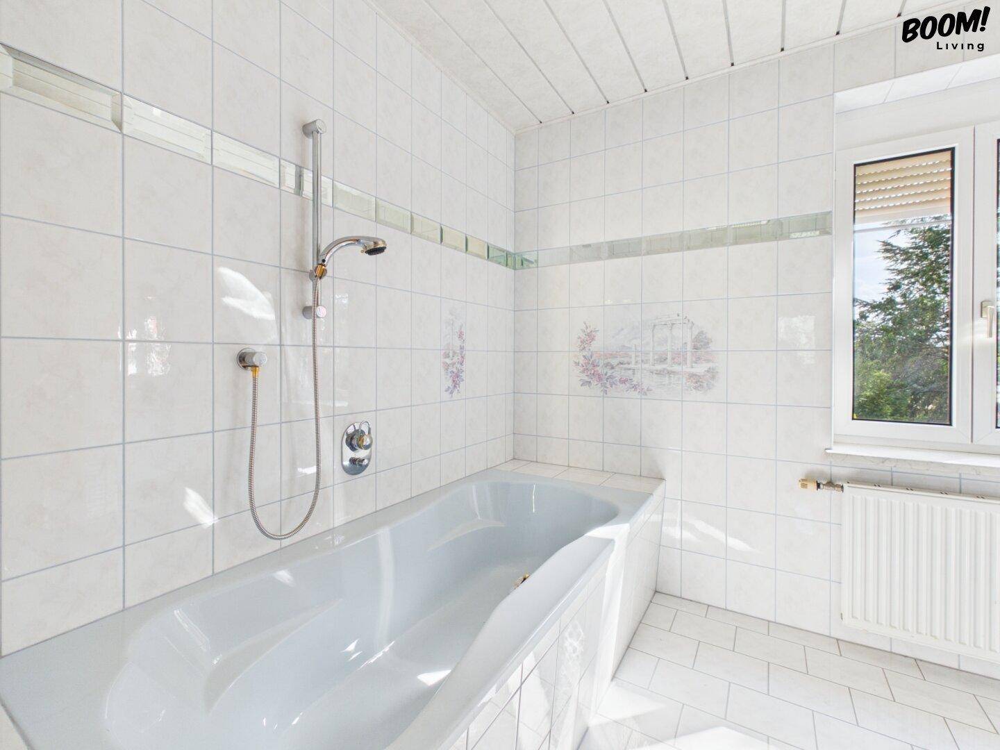 Helles Badezimmer mit Badewanne, weißen Fliesen und Fenster, bietet eine angenehme Atmosphäre.