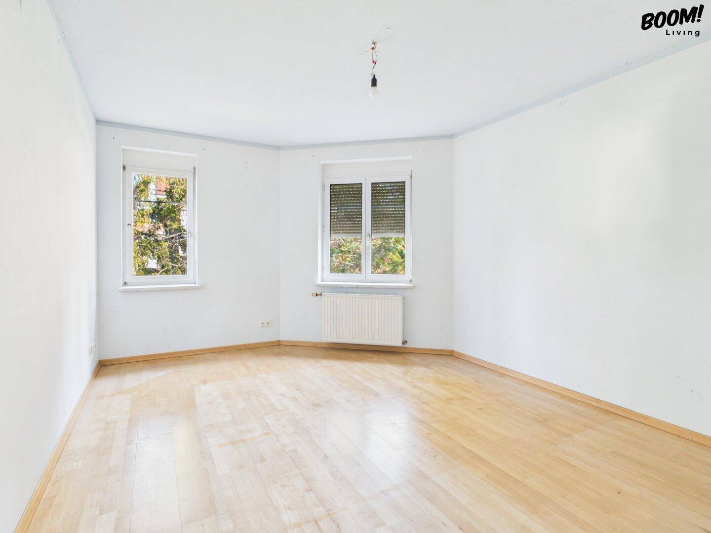 Helles Schlafzimmer mit Parkettboden und zwei Fenstern, bietet viel Potenzial zur individuellen Gestaltung.