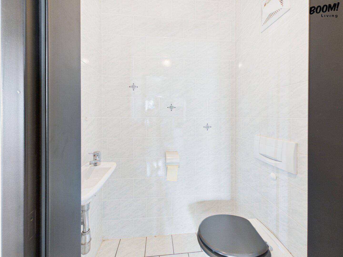 Kleines Gäste-WC mit weißen Fliesen, wandhängendem WC und Handwaschbecken.