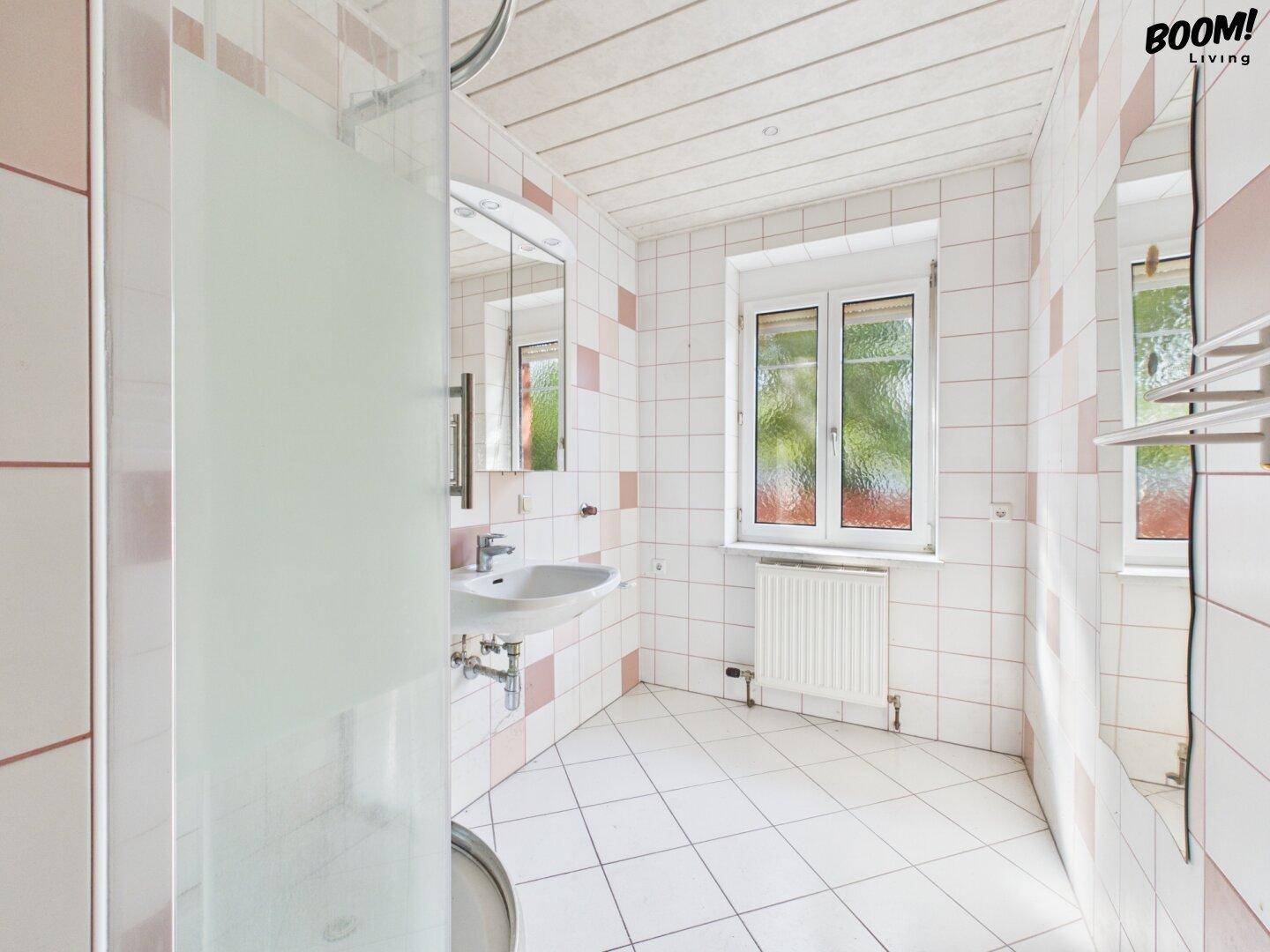 Badezimmer mit Duschkabine, Waschbecken und Spiegel, gefliest in Weiß und Rosa.