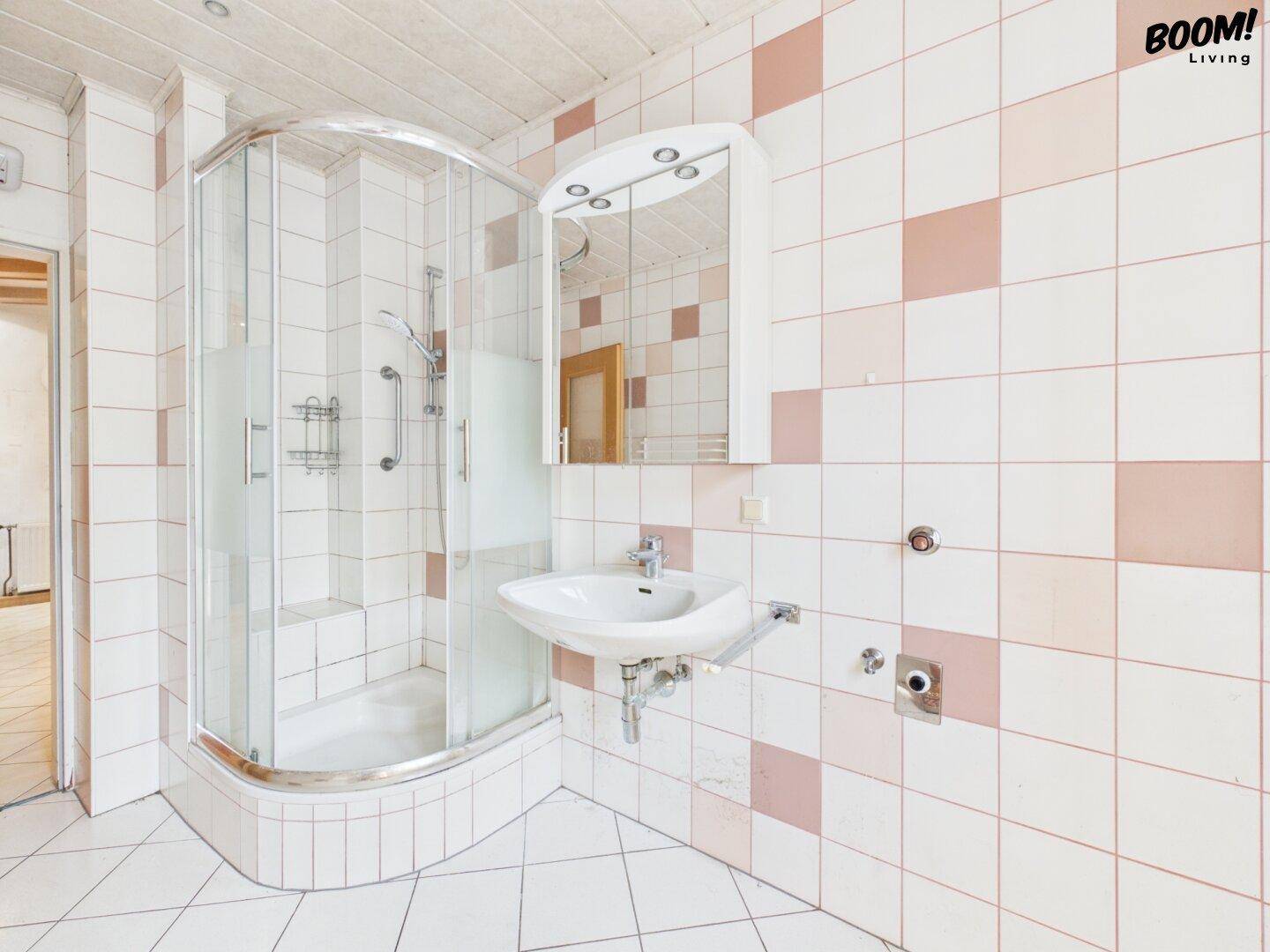 Badezimmer mit Duschkabine, Waschbecken und Spiegel, gefliest in Weiß und Rosa.