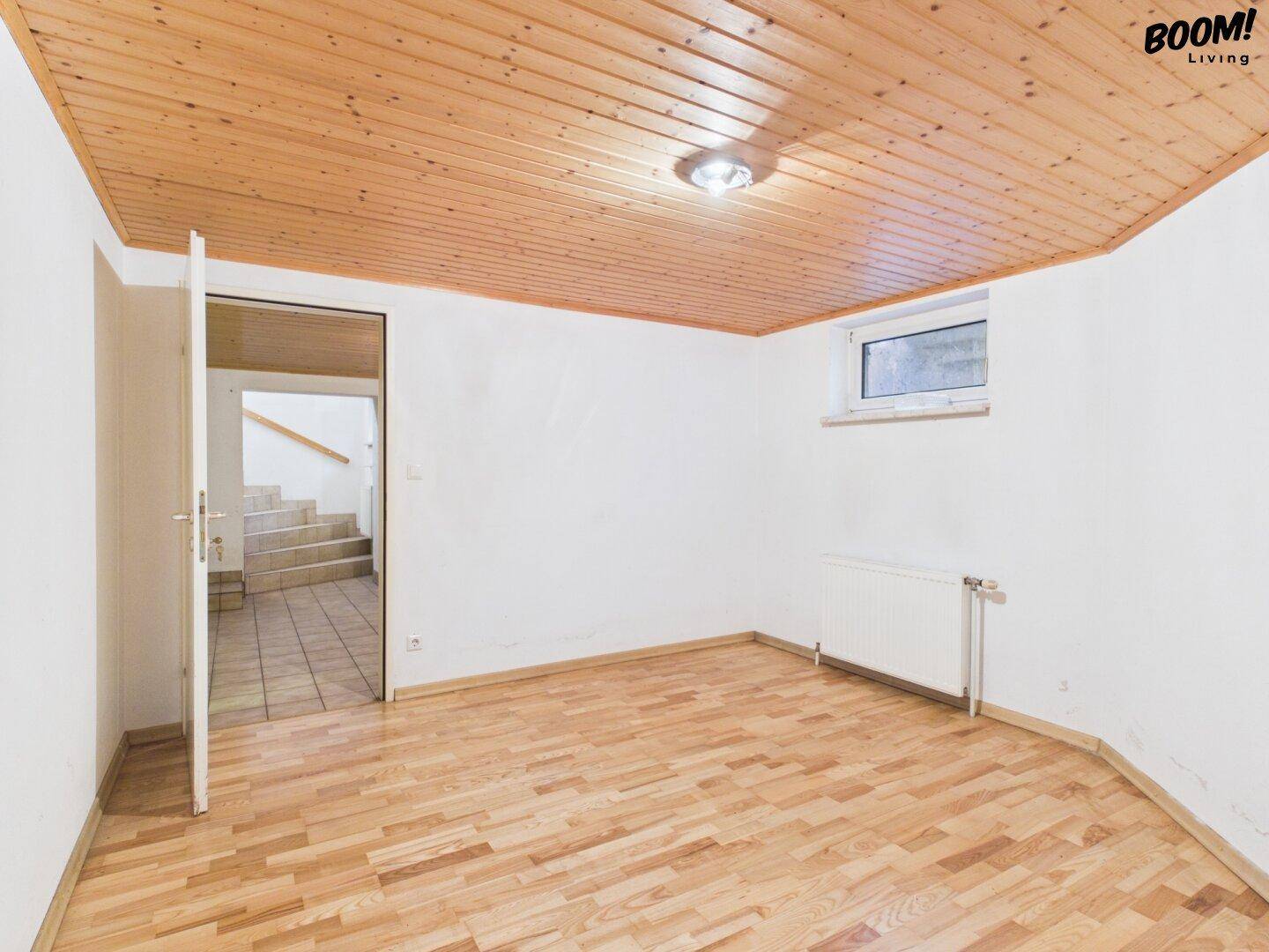 Heller Raum im Untergeschoss mit Holzparkettboden, Holzdecke und Zugang zum Treppenhaus.