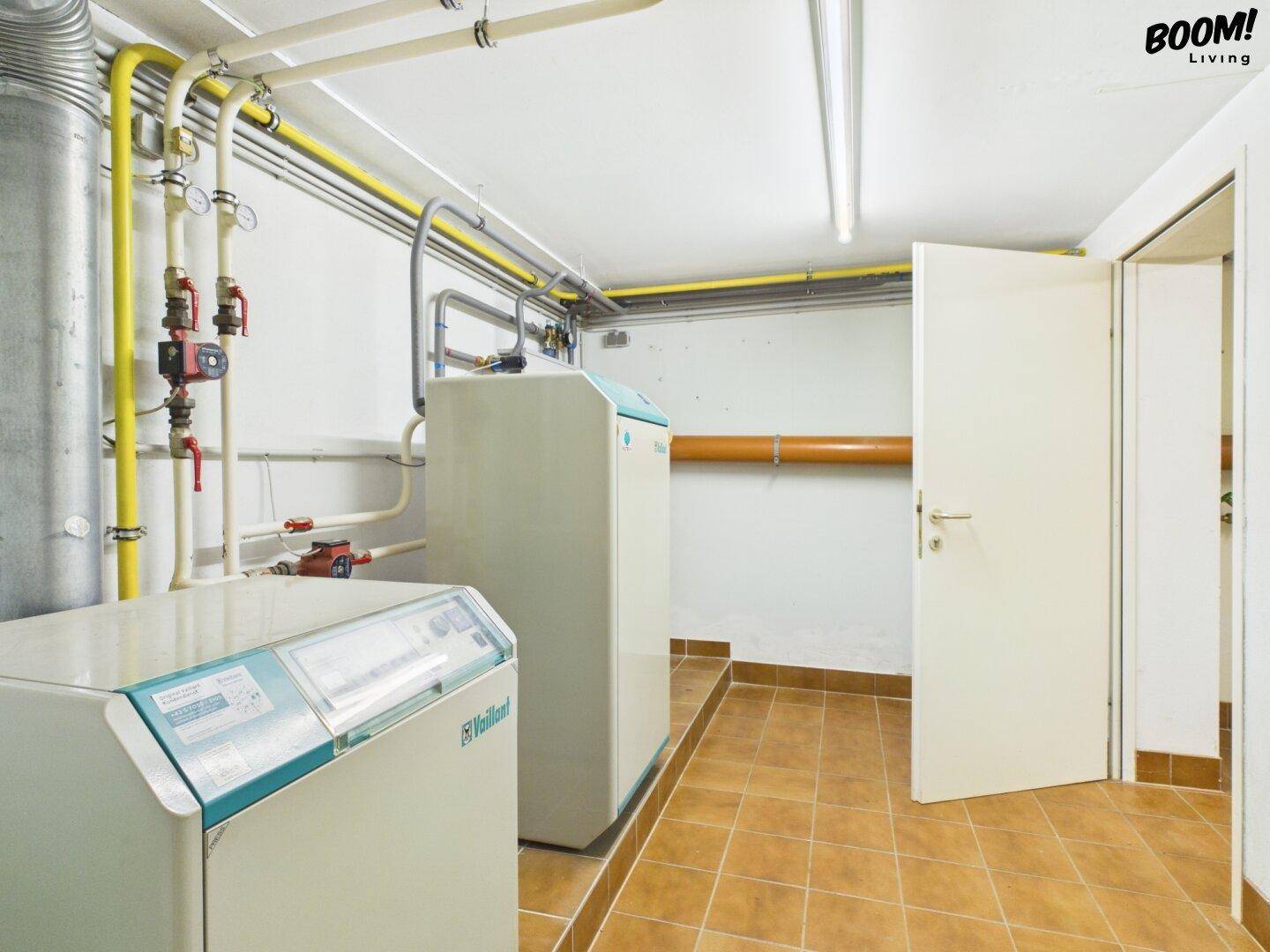 Heizungsraum im Keller mit technischen Anlagen, Rohren und gefliestem Boden.