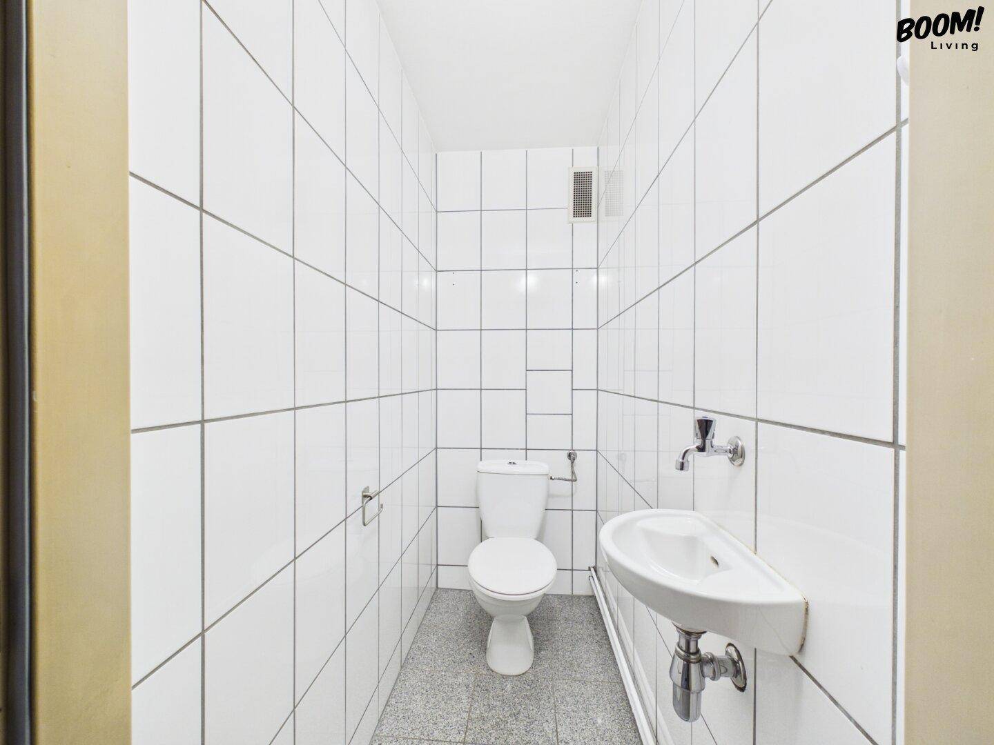 Separates WC mit weißen Fliesen, Toilette und kleinem Handwaschbecken, funktional und sauber.