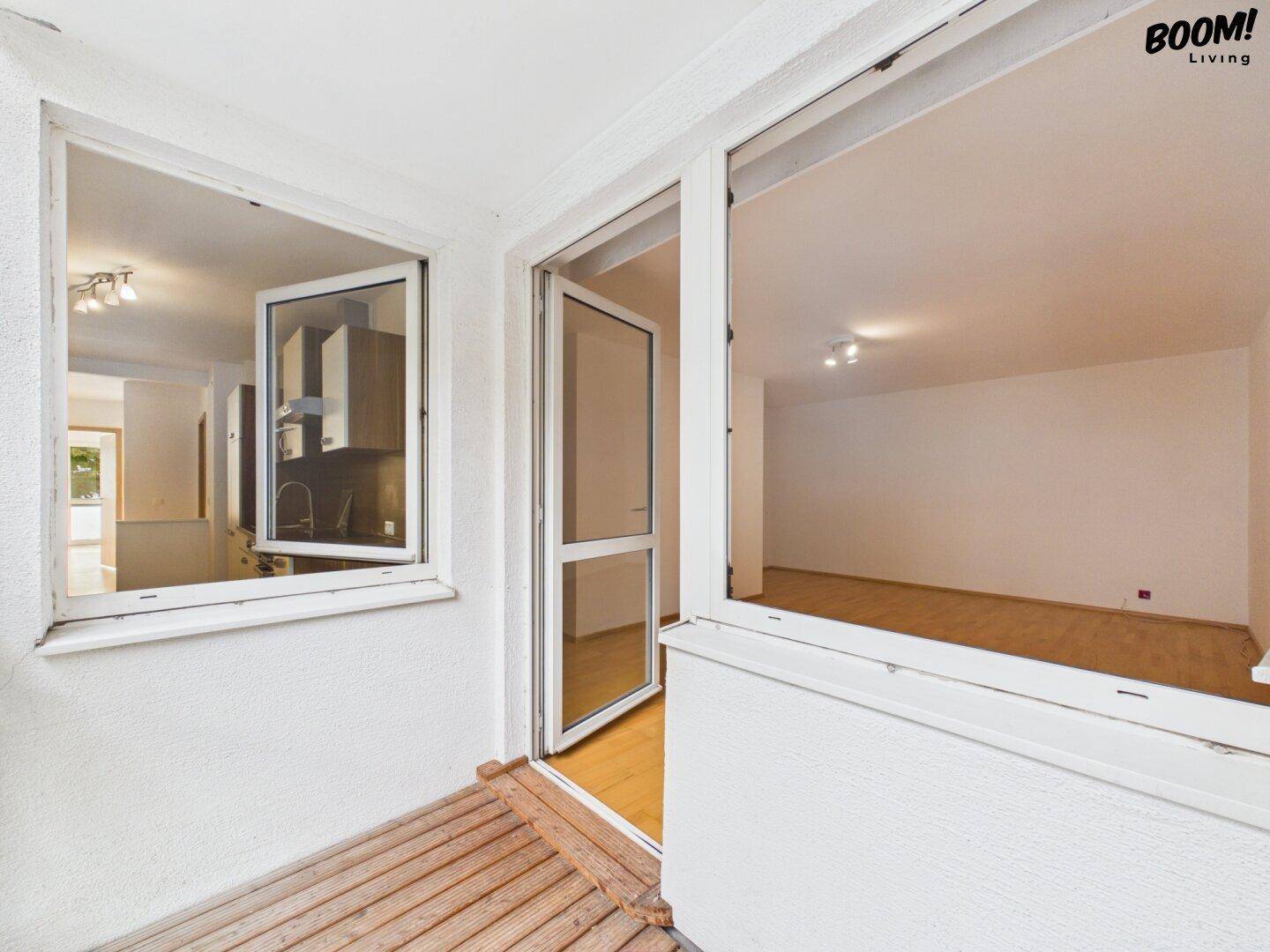 Blick von einem Balkon mit Holzbelag in die hellen Innenräume der Wohnung.