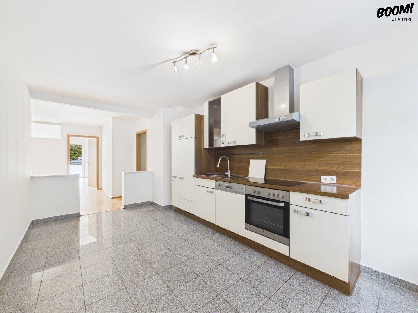 Funktionale Küche mit weißen Schränken, Holzdetails und Fliesenboden, blick in den Flur.