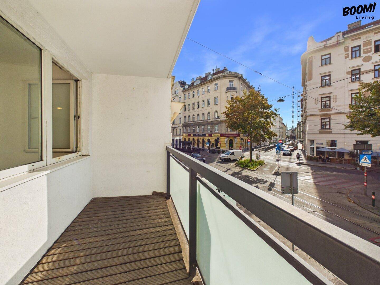 Balkon mit Holzbelag und Glasgeländer bietet einen weiten Blick auf die belebte Stadtstraße.