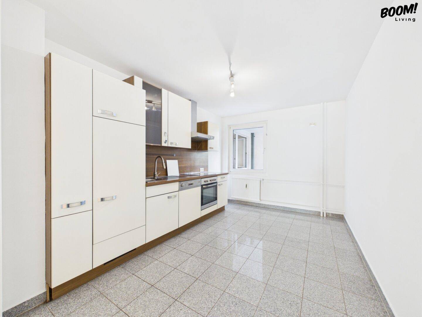 Geräumige Küche mit Einbauküche, Fliesenboden und Fenster, bereit für einen Essbereich.