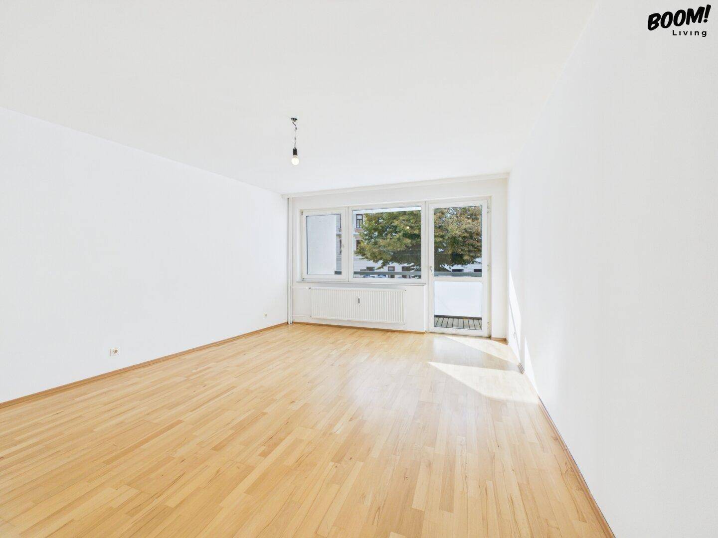 Lichtdurchflutetes Wohnzimmer mit Parkettboden und großem Fenster mit Balkonzugang.